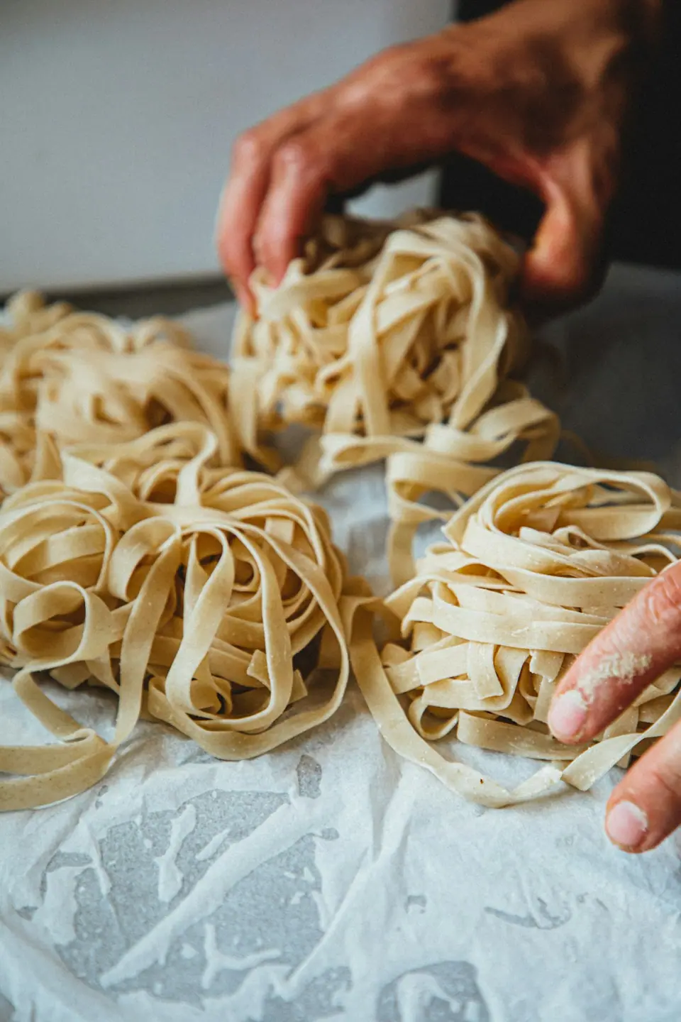 Hands shaping nests of fresh ribbon pasta