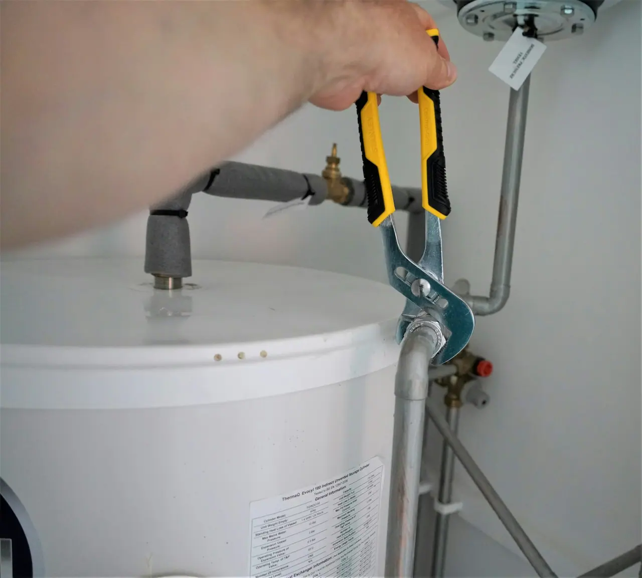 A plumber tightening a fitting on a water heater with pliers